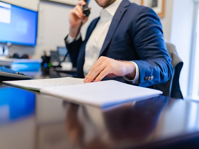 man in business suit at a desk on the phone with a hand on a notebook
